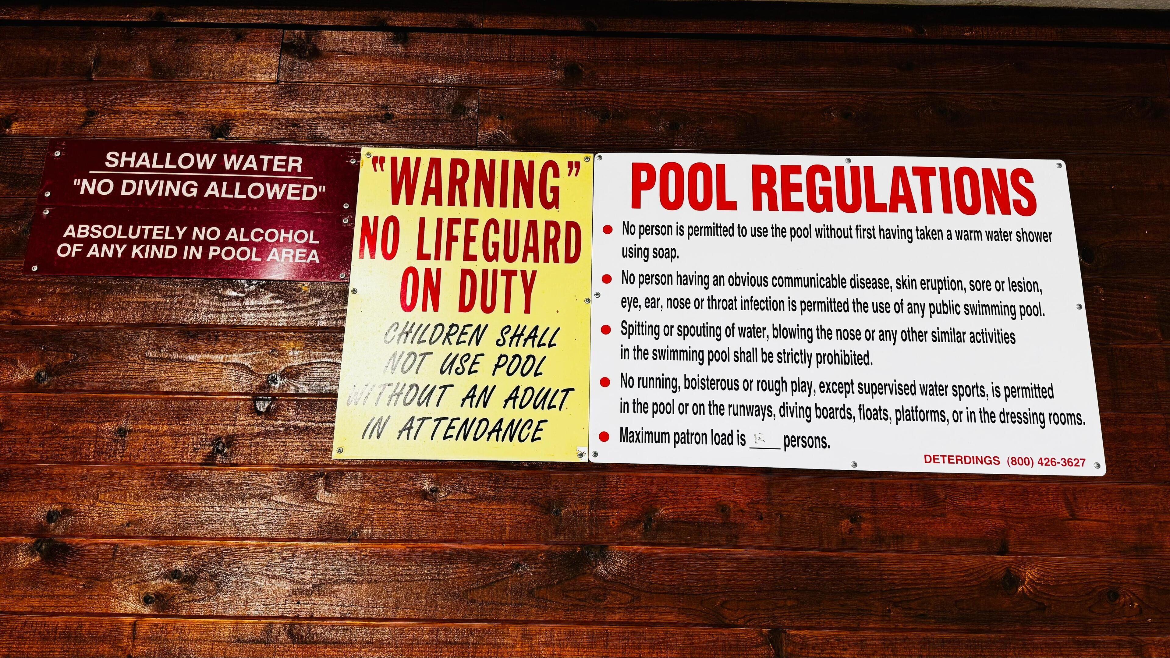 A wooden wall with multiple safety and pool usage signs.