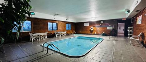Una piscina interior con suelo de baldosas, paredes de madera y sillas de plástico blanco alrededor de la zona de la piscina.