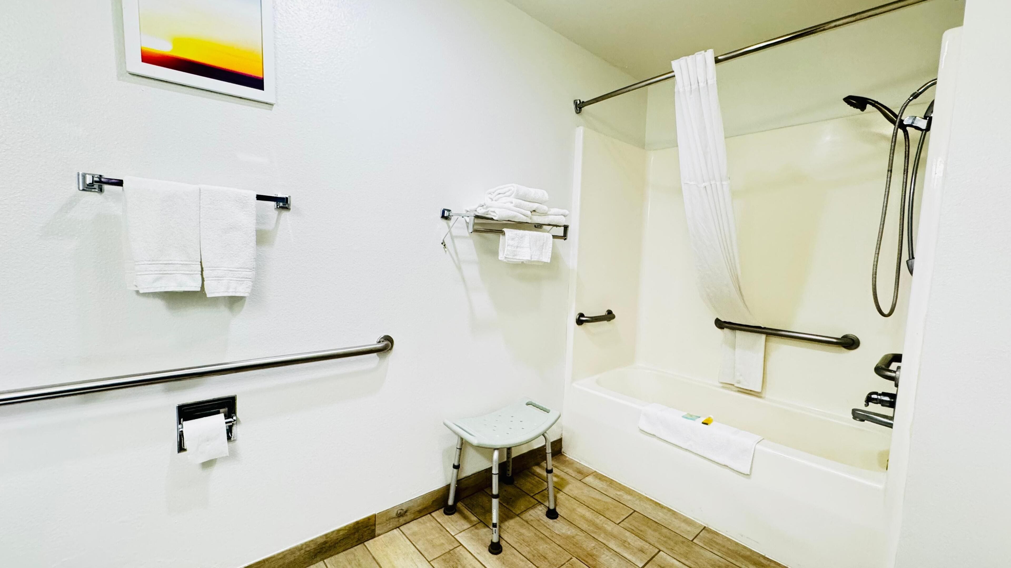 A bathroom with a shower, grab bars, a small step stool, and multiple towels.