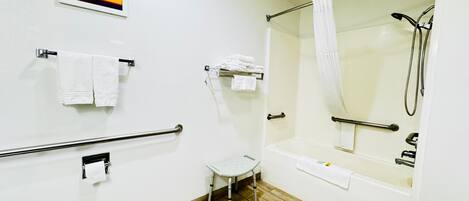 A bathroom with a shower, grab bars, a small step stool, and multiple towels.