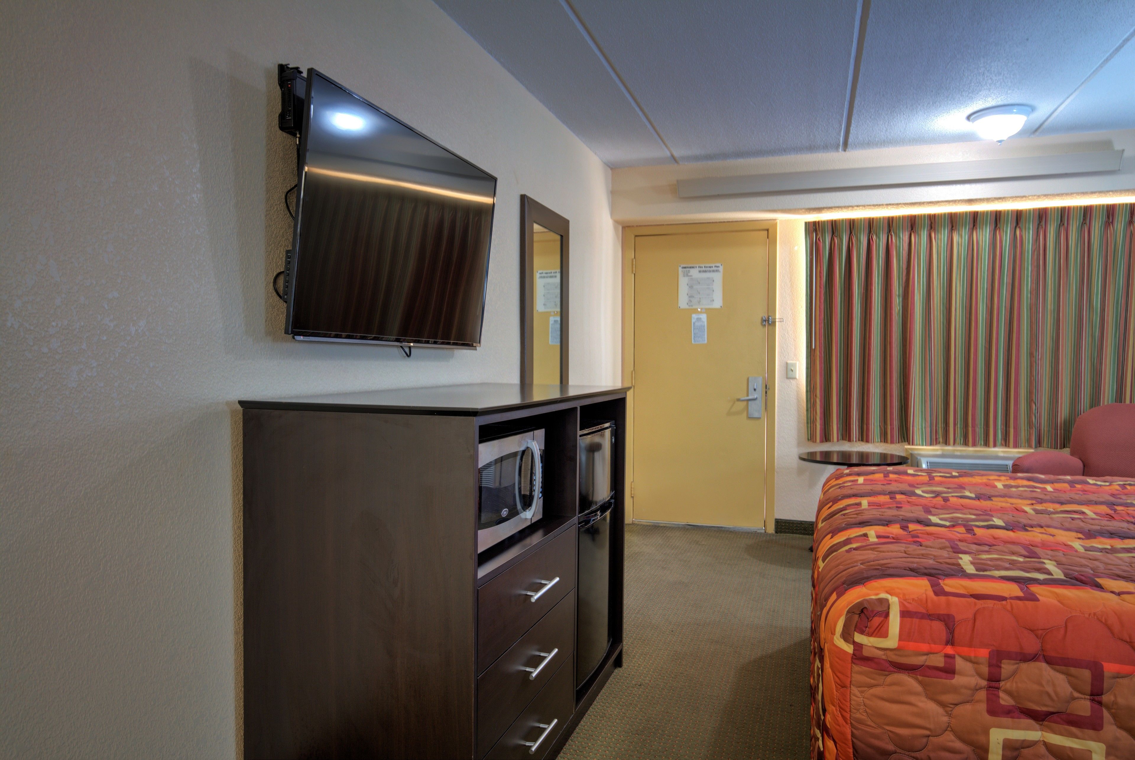 Une chambre d’hôtel avec un lit, un téléviseur fixé au mur, un four à micro-ondes et une petite table avec une chaise.