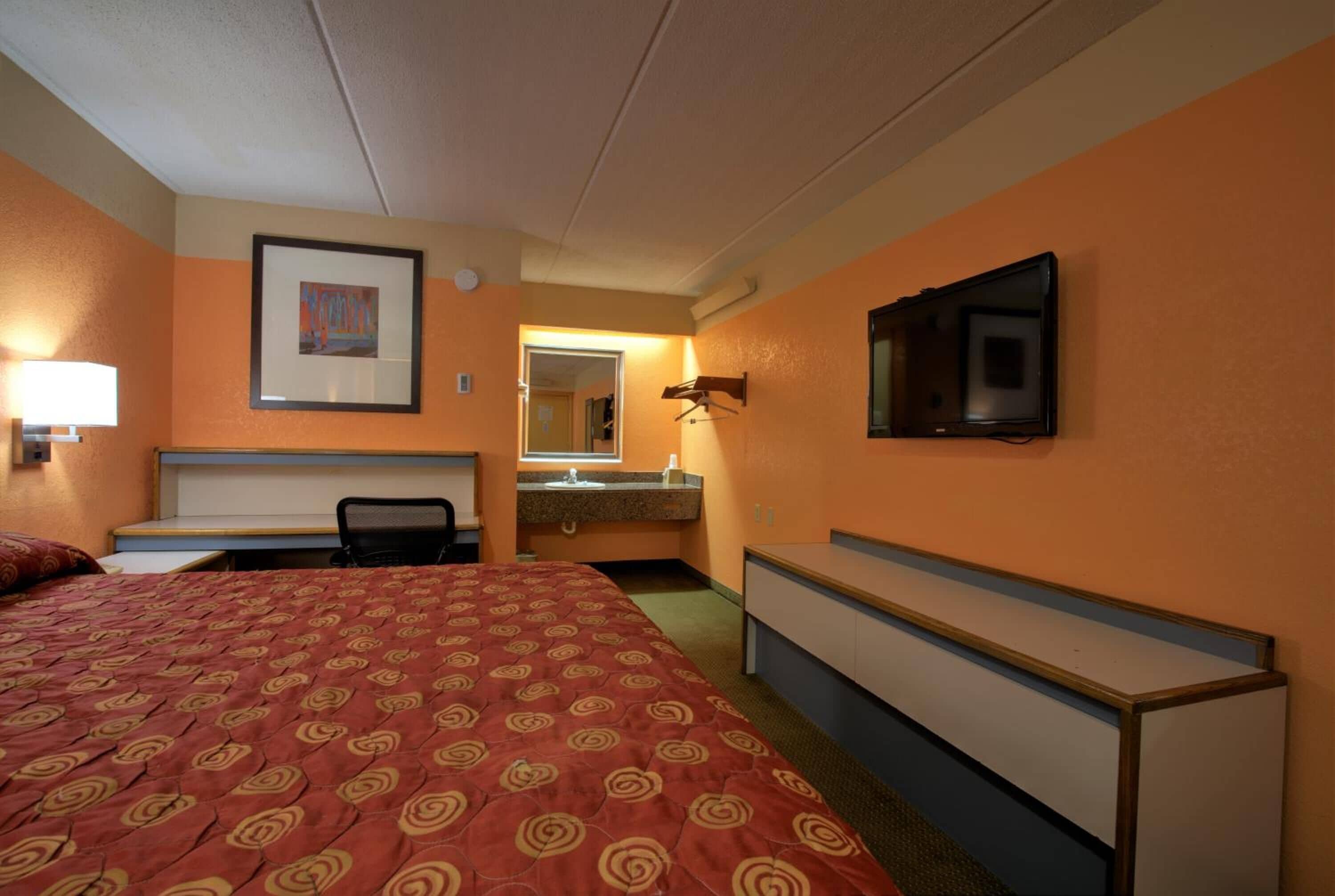 A hotel room with a large bed, a desk, a chair, a television mounted on the wall, and a bathroom visible through an open door.