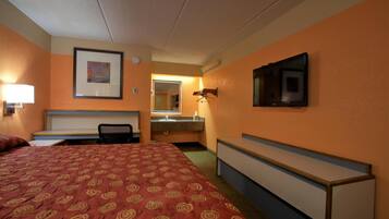 A hotel room with a large bed, a desk, a chair, a television mounted on the wall, and a bathroom visible through an open door.