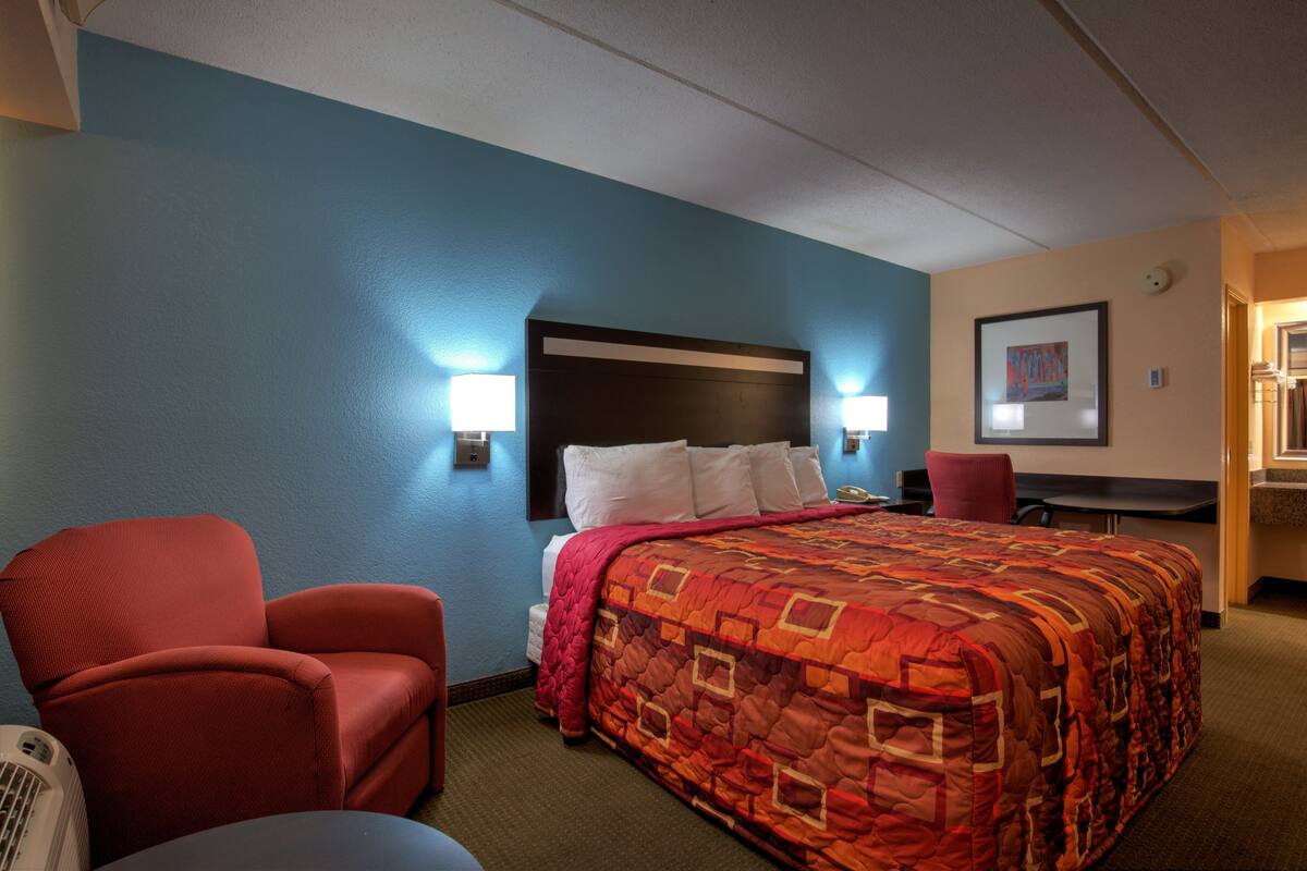 Una habitación de hotel con una cama, un sillón rojo, un escritorio y una silla.