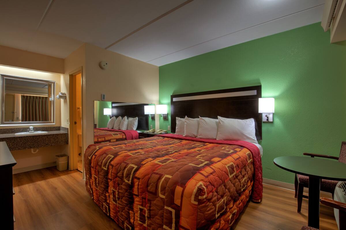 Habitación de hotel con dos camas, una pared verde, piso de madera, baño con lavamanos y un pequeño comedor.