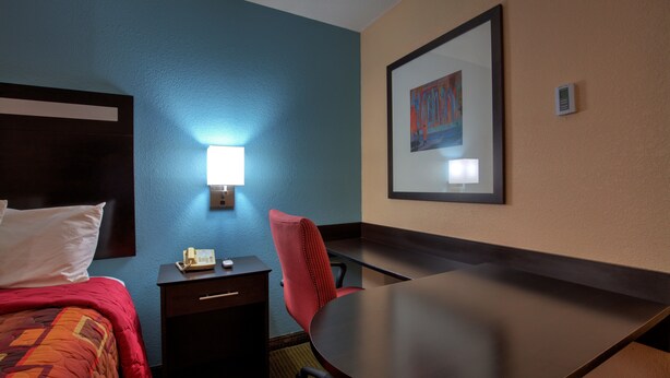 Habitación de hotel con cama, escritorio, silla, teléfono y un cuadro en la pared.