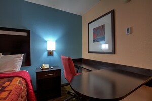 Habitación de hotel con cama, escritorio, silla, teléfono y un cuadro en la pared.