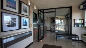 Un vestíbulo de hotel con cuadros enmarcados en la pared, un mostrador de recepción, un banco y una puerta de cristal que da a otra zona.