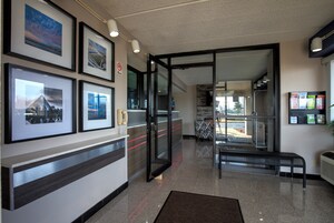 Un vestíbulo de hotel con cuadros enmarcados en la pared, un mostrador de recepción, un banco y una puerta de cristal que da a otra zona.