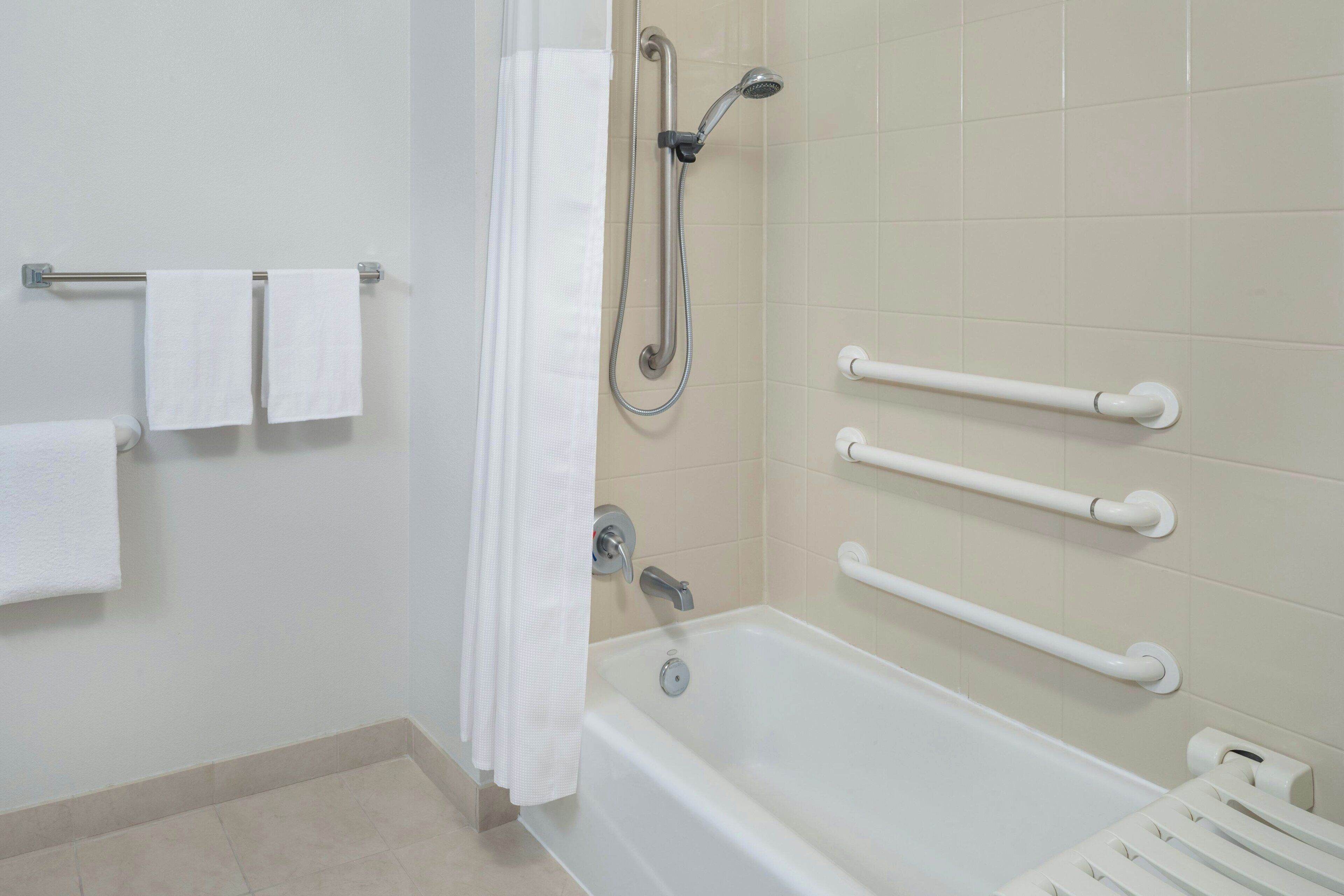 A bathroom with a bathtub, grab bars, and a towel rack.