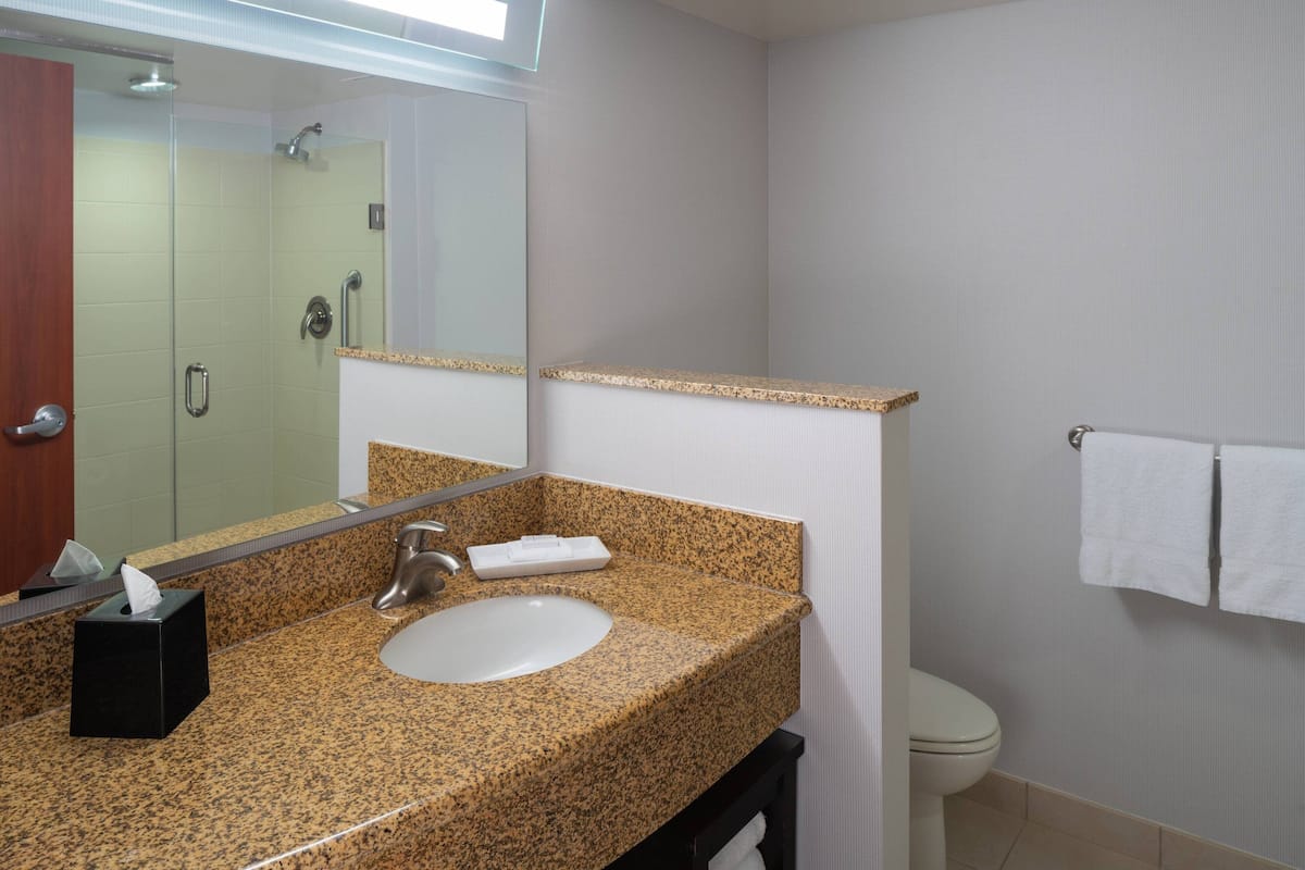 A bathroom with a granite countertop sink, a mirror, a towel rack, and a toilet.