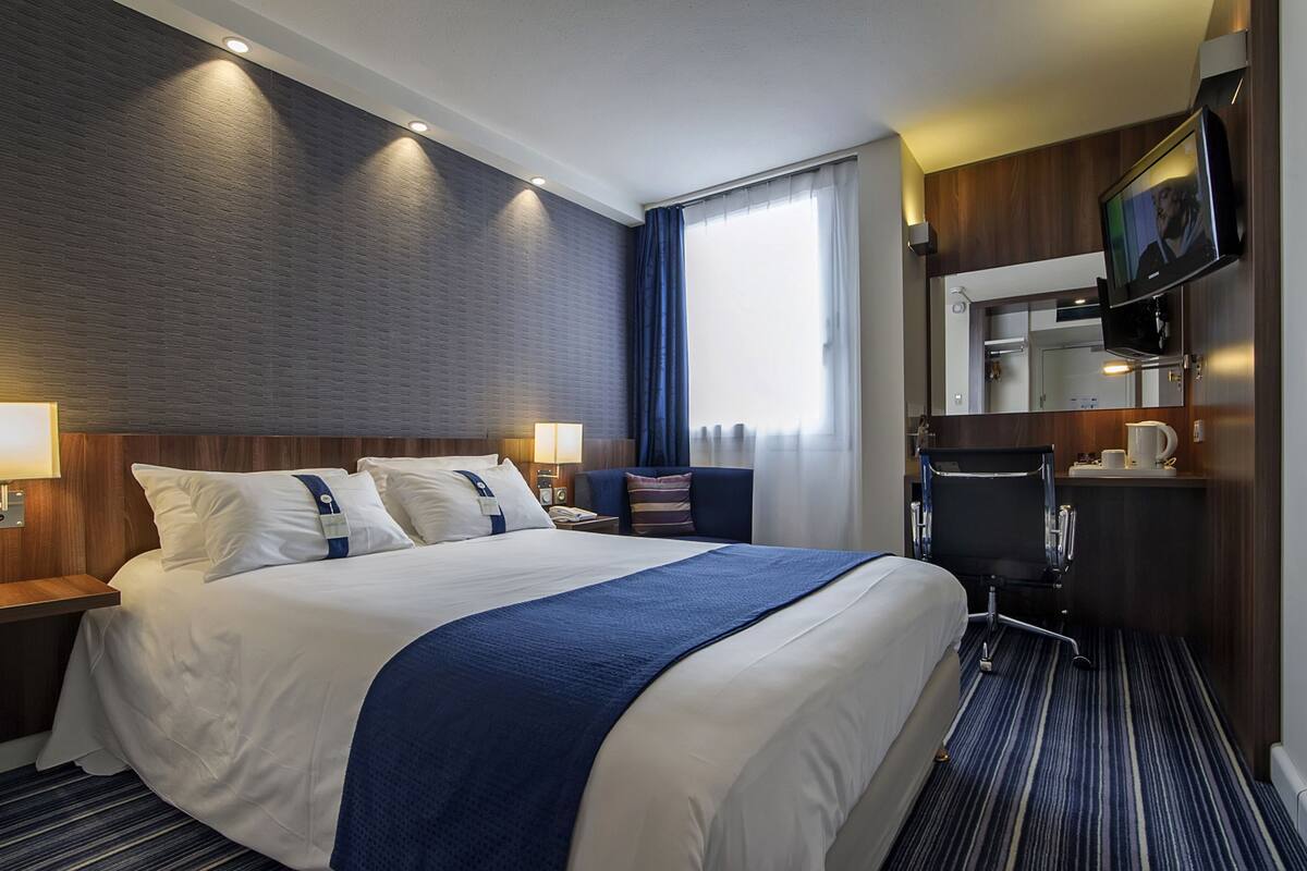 Una habitación de hotel con una cama grande, dos mesitas de noche, un televisor y un espejo de baño.
