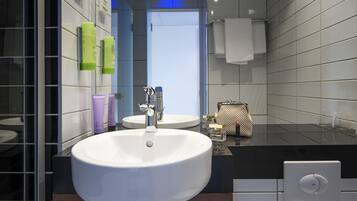 A modern bathroom with a large white sink, a mirror, and toiletries on the wall.