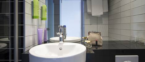 Un baño moderno con un lavamanos blanco grande, un espejo y artículos de tocador en la pared.