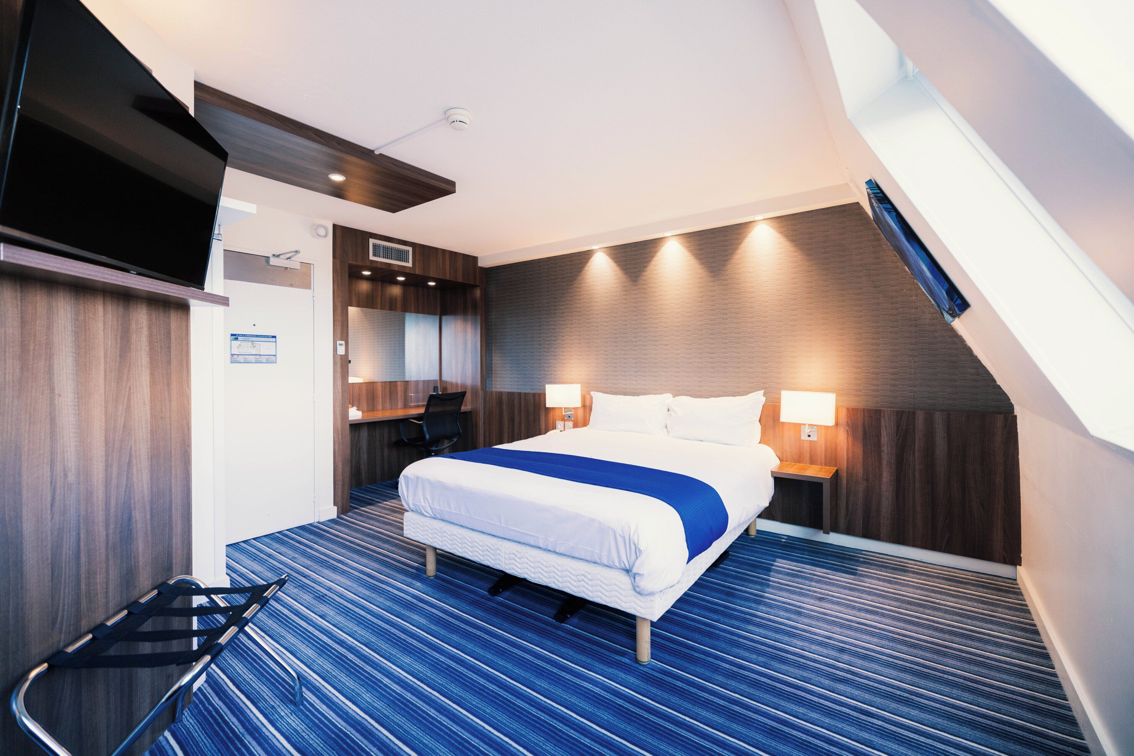 A modern hotel room with a large bed, a desk, and a chair.