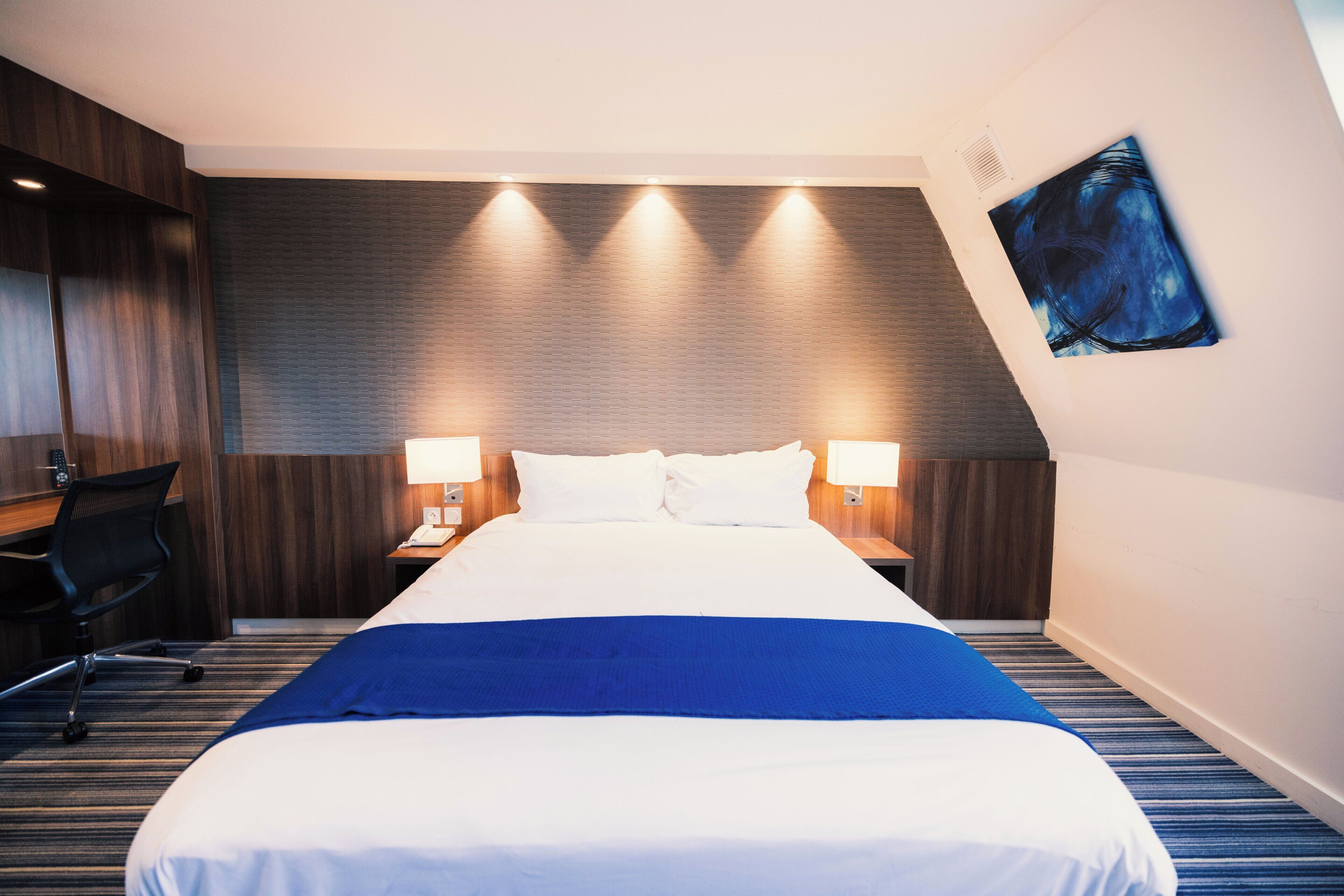 Een hotelkamer met een groot bed, twee nachtkastjes met lampen, een bureau en een stoel.