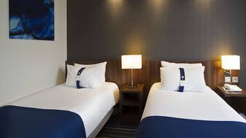 A hotel room with two beds, each with a pillow and a lamp. There is a painting on the wall and a wooden headboard.