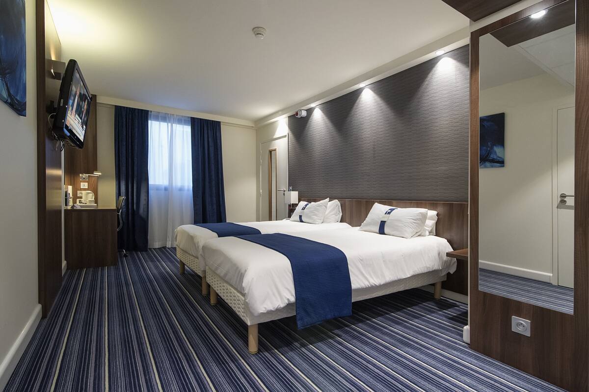 Una habitación de hotel con dos camas, televisión, escritorio y espejo.