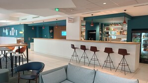 Zona de bar moderna amb taulell de recepció, tamborets i un espai d'estar amb un sofà i cadires.