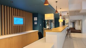 Una zona d'entrada moderna amb un taulell de recepció de fusta, un panell informatiu digital i una zona de bar amb tamborets.