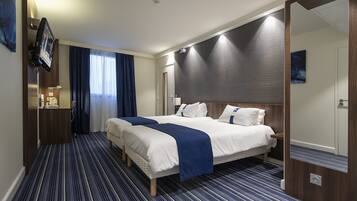 Una habitación de hotel con dos camas, televisor, espejo y ventana con cortinas.