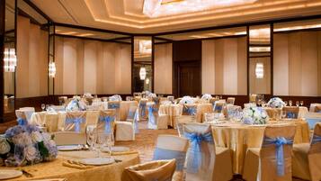 A banquet hall with round tables set for a formal event, featuring white and gold tablecloths, chairs with blue sashes, and floral centerpieces.