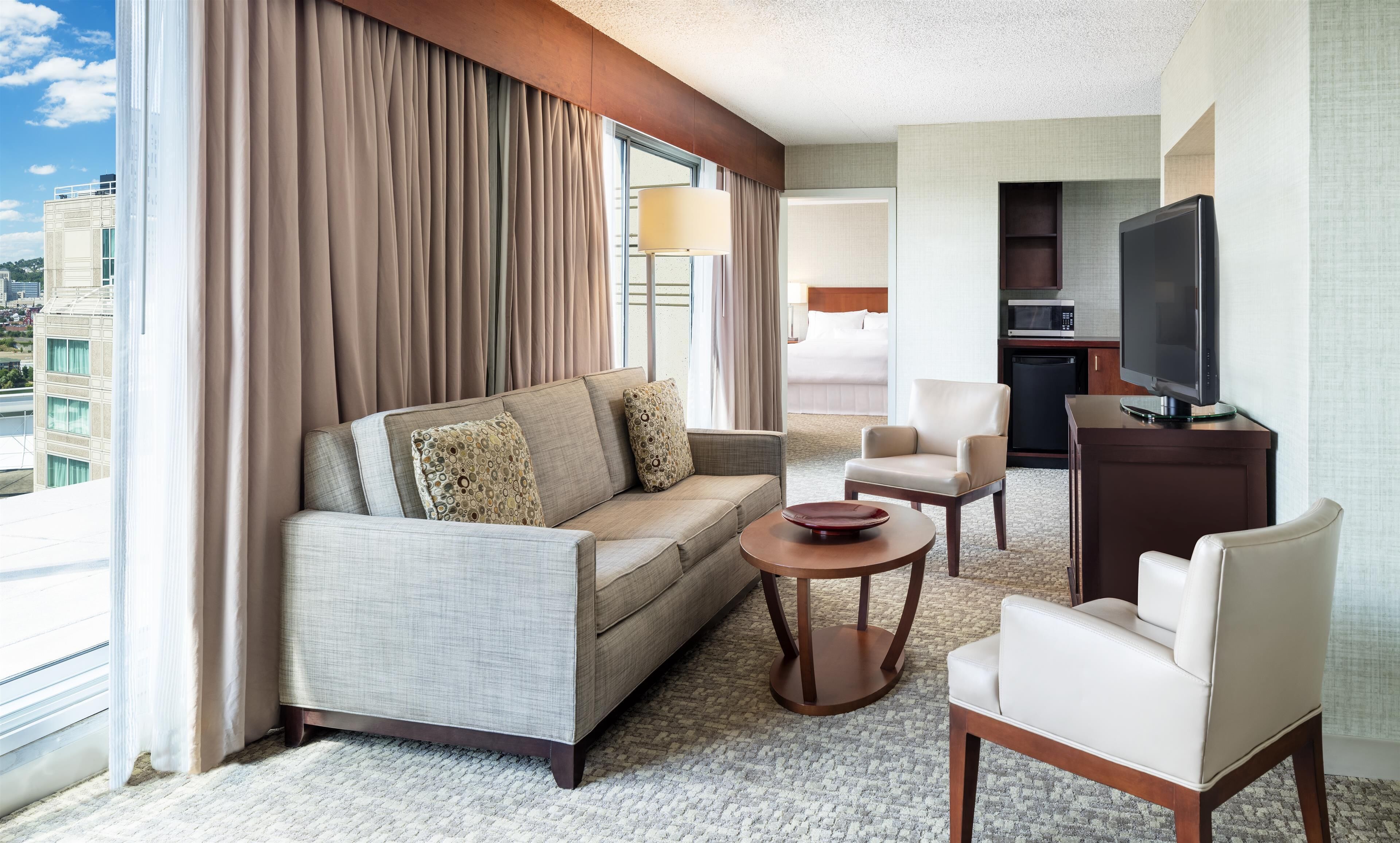 Une chambre d’hôtel équipée d’un canapé, de fauteuils, d’une petite table, d’une télévision et d’une kitchenette.