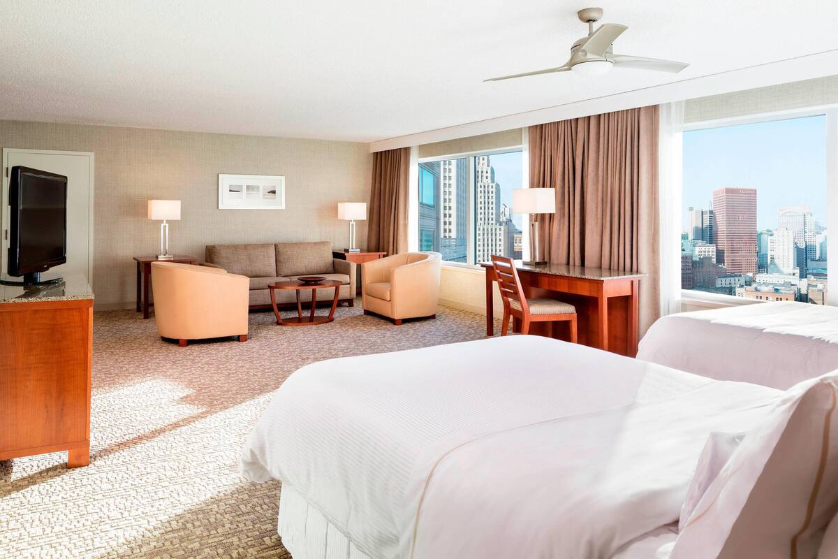 A hotel room with a bed, a desk, a chair, a sofa, a TV, and a city view.