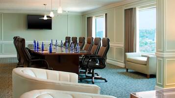 A conference room with a long table, multiple chairs, a TV on the wall, and a view through large windows.