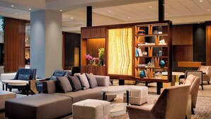 A modern hotel lobby with a sectional sofa, ottomans, armchairs, a wooden bookshelf, and a patterned carpet. - The Westin Pittsburgh, a Marriott Hotel (Pittsburgh)