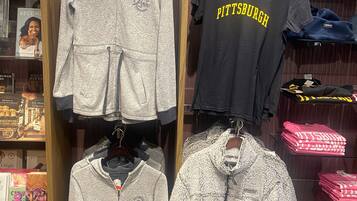 A clothing store with various garments on display, including a grey hoodie and a black t-shirt with 'Pittsburgh' written on it.