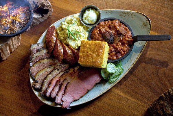 A plate of sliced ham, beans, cornbread, and a small bowl of sauce.