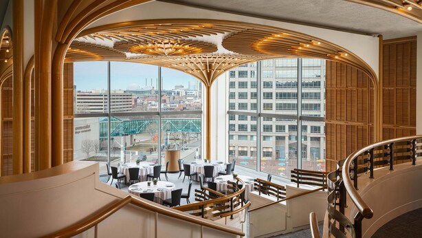 A modern interior with a curved wooden ceiling, large windows offering city views, and a dining area with round tables and chairs. - Sheraton Kansas City Hotel at Crown Center (Kansas City)