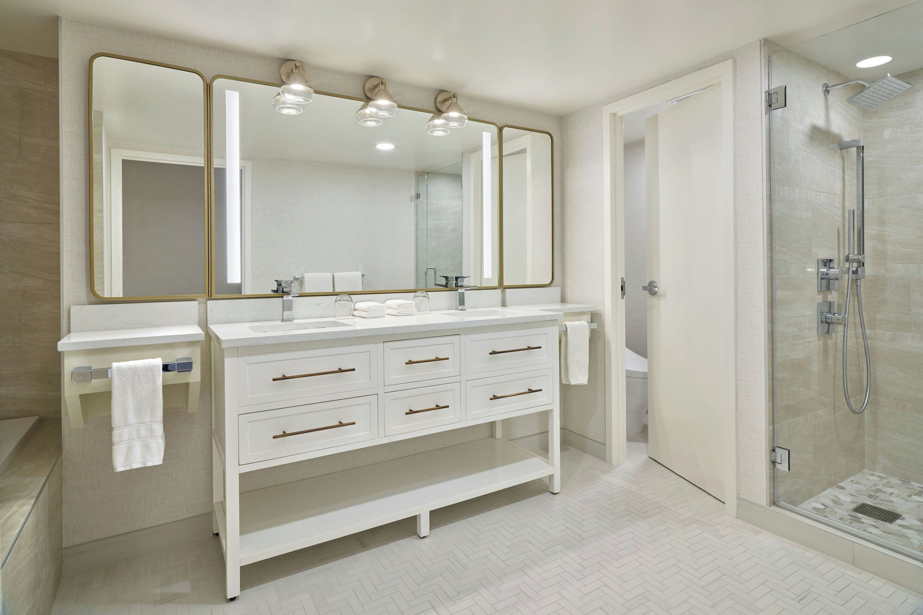 A modern bathroom with a double sink vanity, a large mirror, and a walk-in shower.