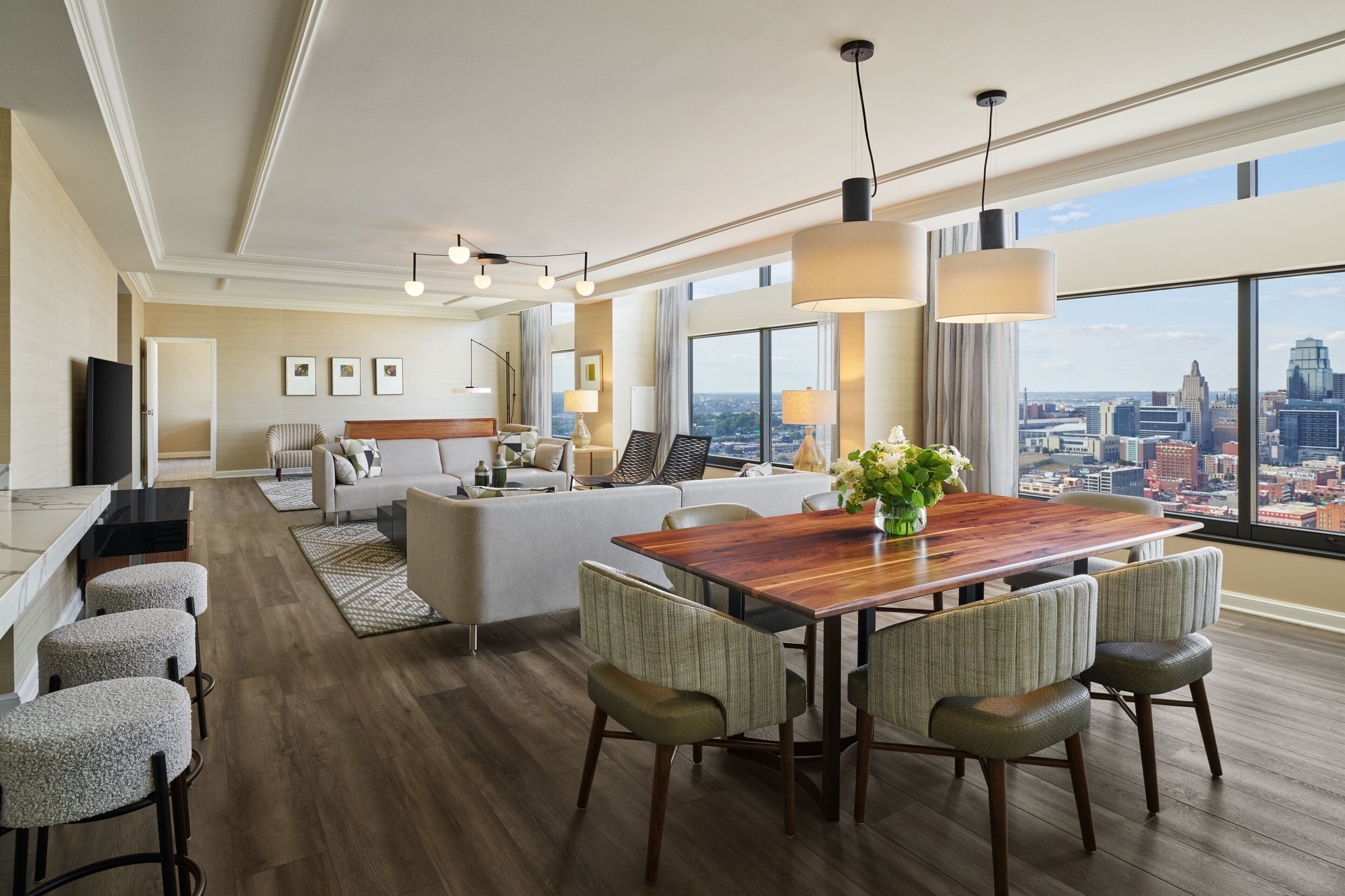 A modern hotel room with a dining area, a sofa set, and a city view.