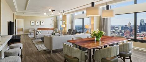 A modern hotel room with a dining area, a sofa set, and a city view.