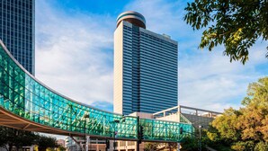 A modern urban scene with a curved glass pedestrian bridge, a tall building with a cylindrical top, and a clear blue sky. - Sheraton Kansas City Hotel at Crown Center (Kansas City)