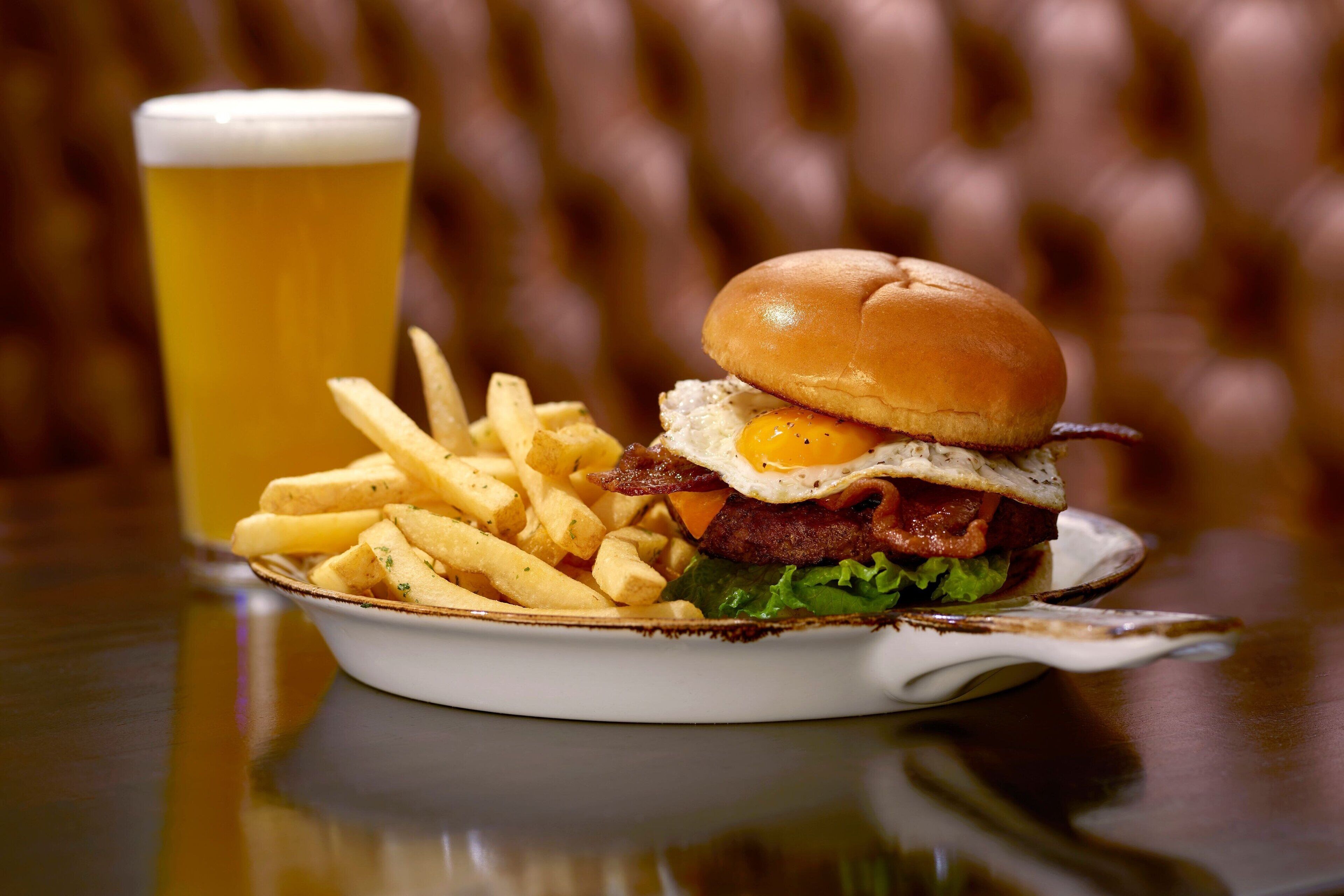 Ein Burger mit Pommes und einem Glas Bier auf einem Tisch.