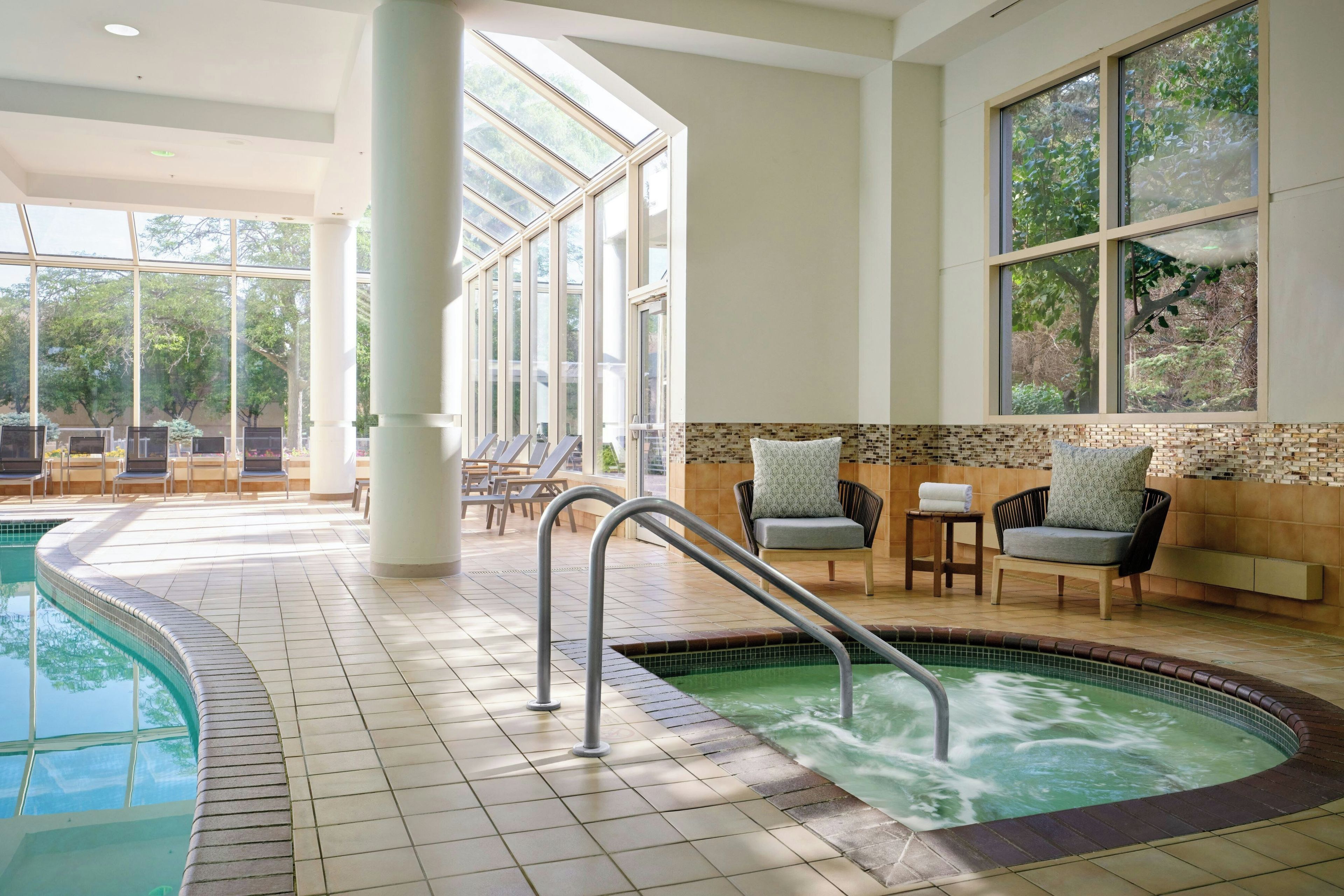 Un espace piscine comprenant un jacuzzi, des chaises longues et une vue sur l’extérieur.