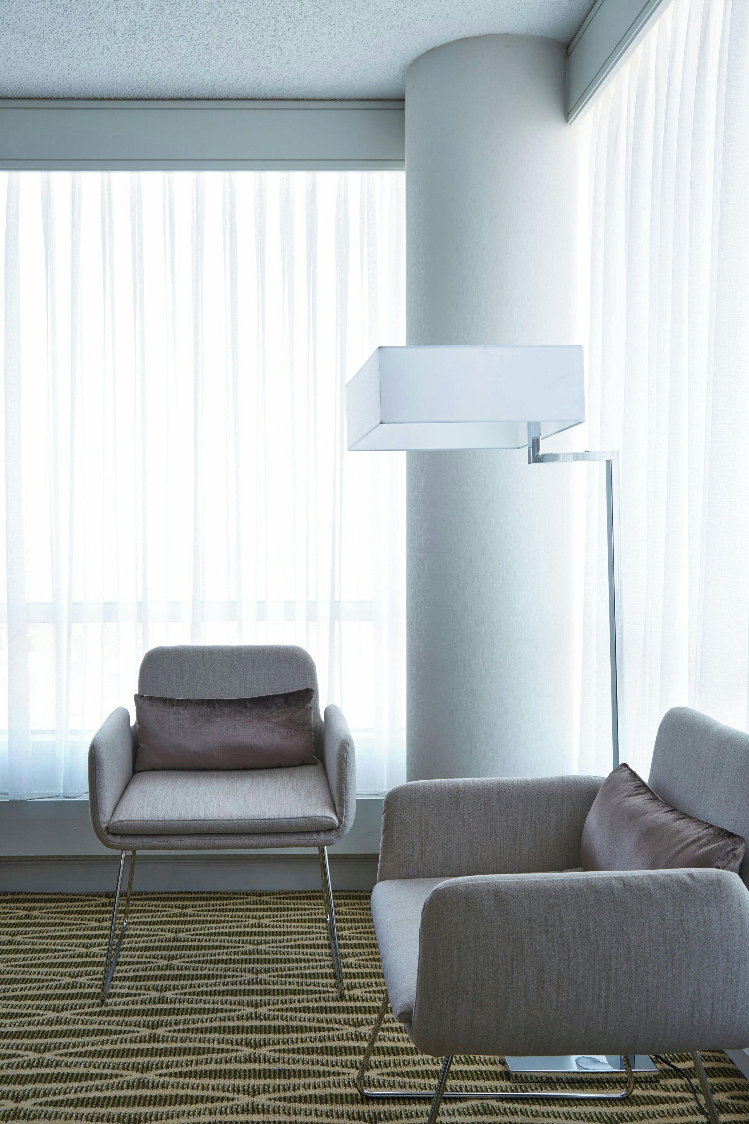 Una habitación moderna con un ventanal grande, una lámpara de pie y dos sillones.