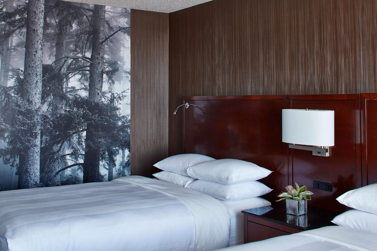 Une chambre d’hôtel avec un grand lit, une table de chevet avec une lampe et une fresque murale représentant une forêt.