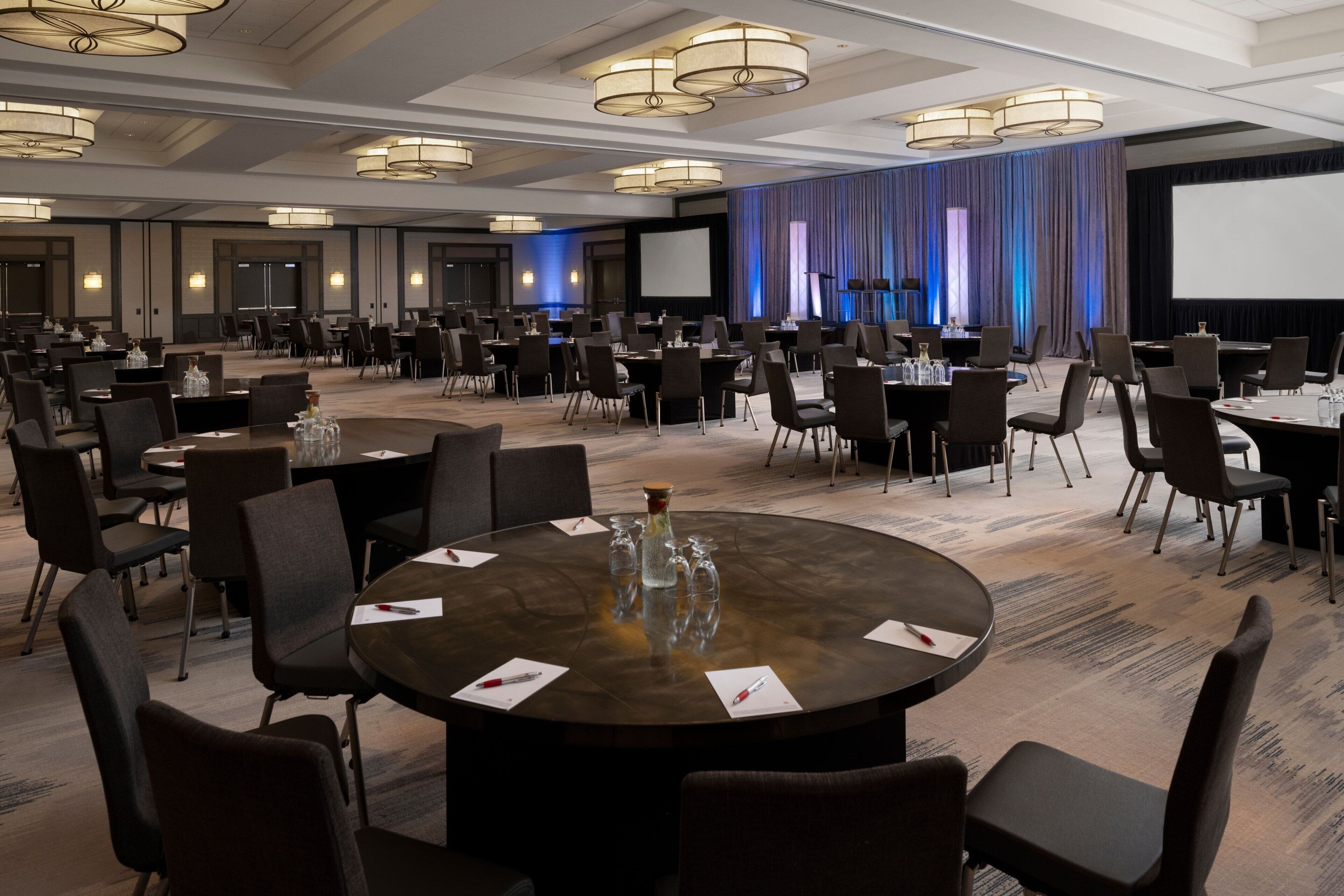 A conference room with round tables, chairs, and a large screen.