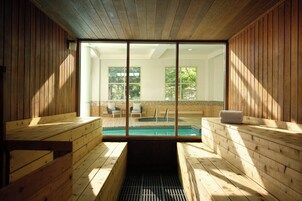 A sauna room with wooden benches, a glass wall, and a view of an outdoor seating area.