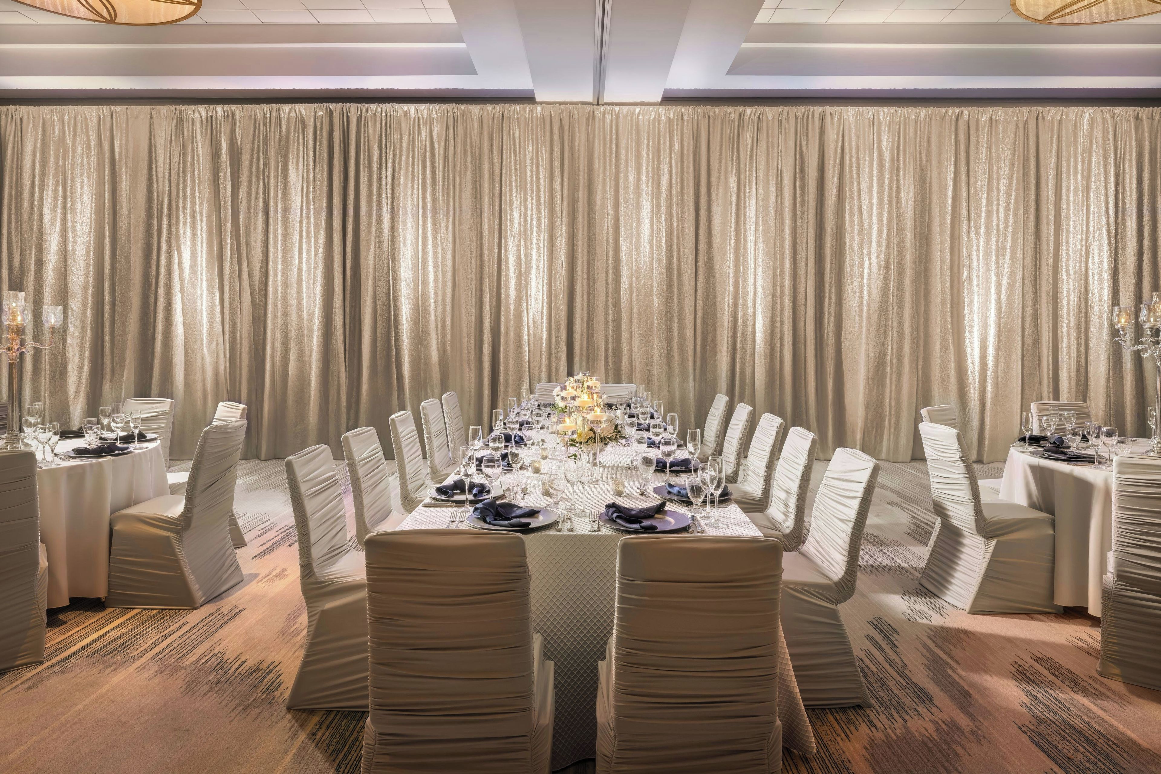 Uma sala de jantar formal com uma longa mesa posta para refeição, com cortinas e lustres.
