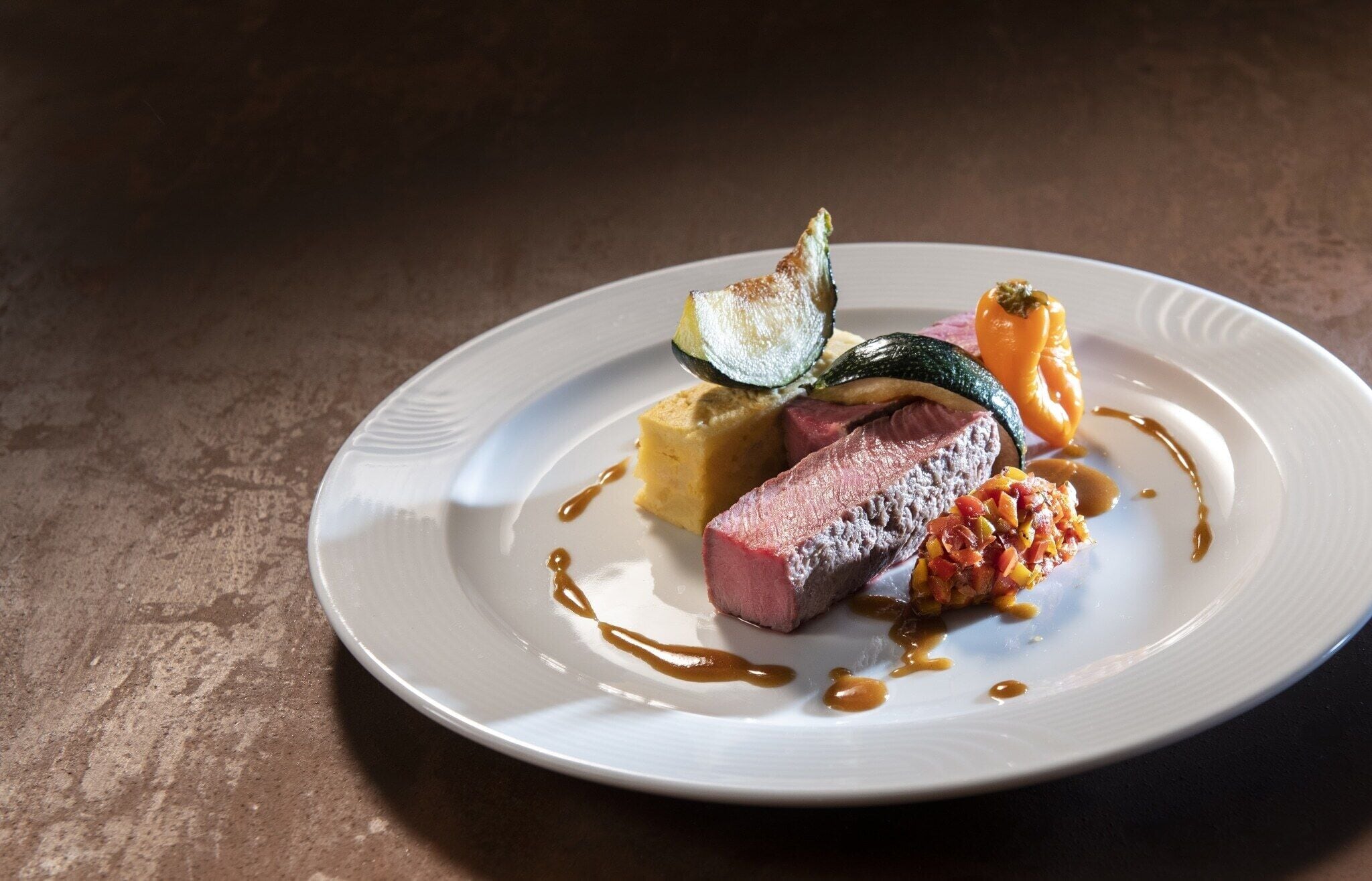 A plate of food with a piece of meat, a vegetable, and a small dish of sauce.