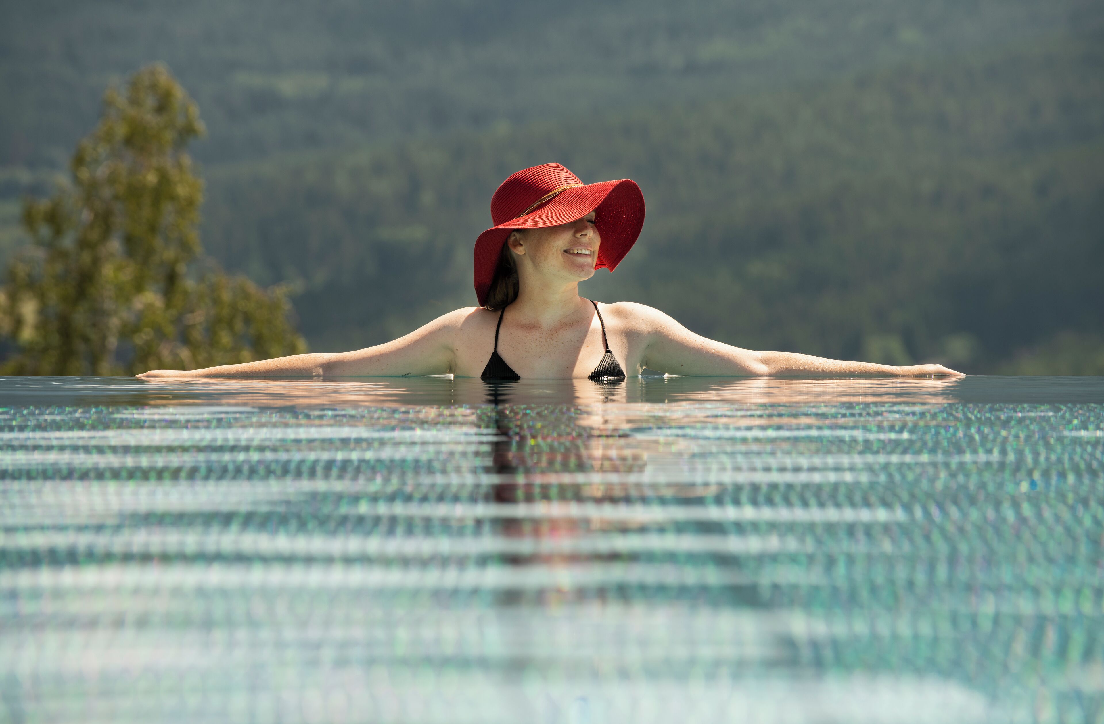A person in a swimming pool with a red hat, surrounded by water and greenery in the background.