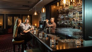 A bar area with a bartender preparing drinks, a seated couple, and a bar stocked with various bottles and glasses.