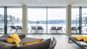 A modern hotel room with large windows, a grey sofa, yellow cushions, and a view of an outdoor pool area.