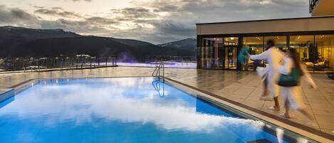 Una piscina con vistas a montañas y un edificio con puertas de cristal.
