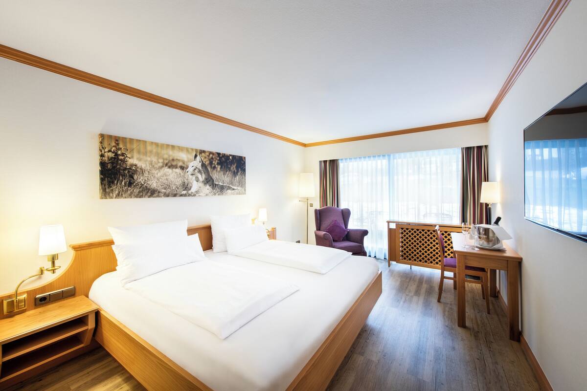 A hotel room with a large bed, a desk, a chair, and a painting on the wall.